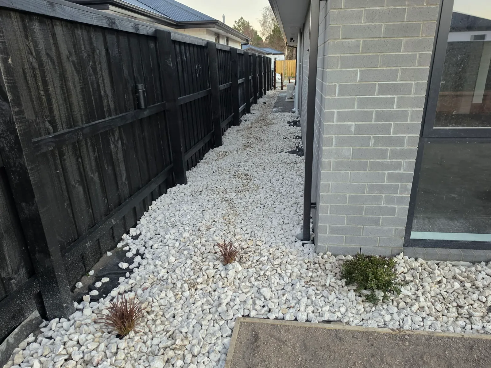 Side access path with decorative white gravel and black timber fence at 25 Derbridge Street, Christchurch